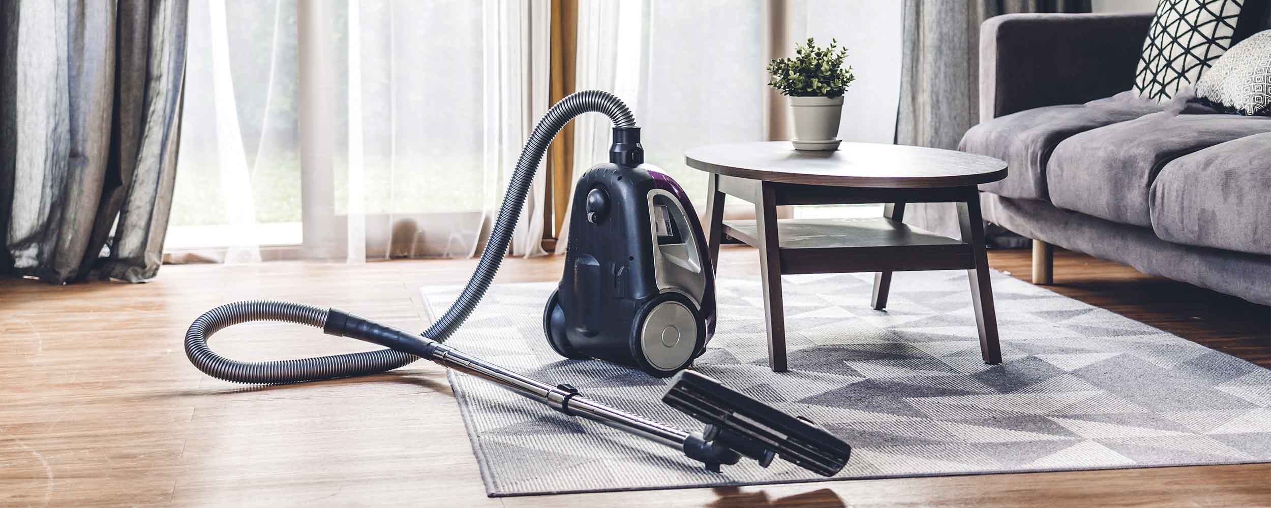Modern upright vacuum cleaner with hose and floor attachment displayed on on a patterned rug in a modern living room, emphasizing premium quality spare parts available